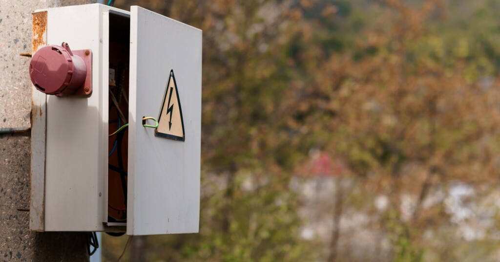 An outdoor metal electrical enclosure with a symbol of a yellow triangle and black bolt on its door and red button on its side.