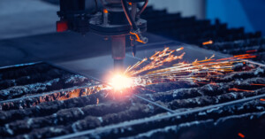 A CNC machine cuts through a piece of metal while bright orange sparks fly outward during the process.