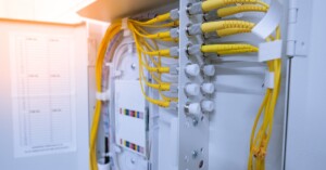 Yellow fiber optic cables connect to ports inside a metal enclosure box with a paper chart fixed to the inside door.