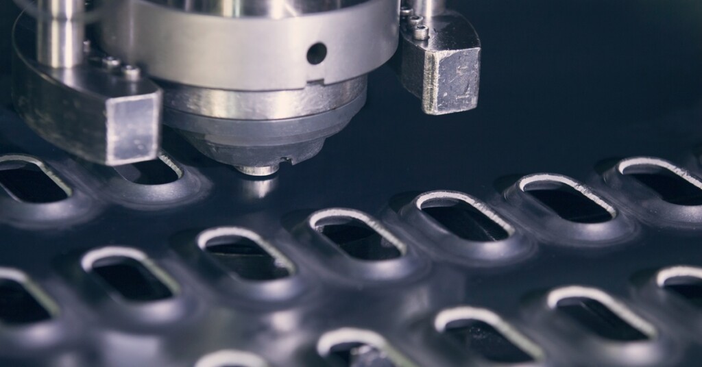 A CNC punching machine perforates a metal sheet with evenly spaced, oval-shaped holes across the surface.