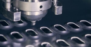 A CNC punching machine perforates a metal sheet with evenly spaced, oval-shaped holes across the surface.