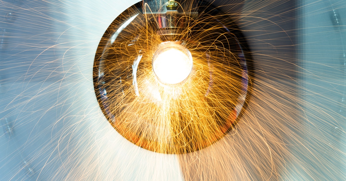 A laser tube cutting machine working on a metal pipe, the center of which glows bright white with heat.