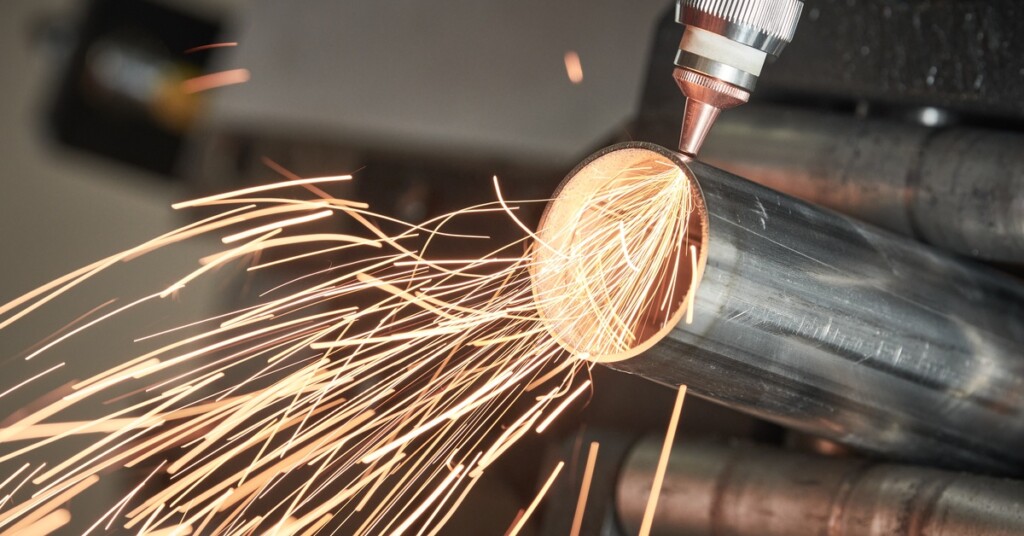 A fiber laser tube cutting machine slicing through a metal pipe and sending yellow sparks outward.