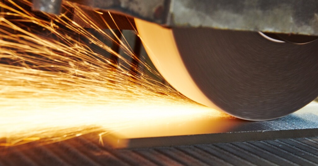 A horizontal grinder machine applies a finish on a metal surface. Sparks fly at the point of contact.