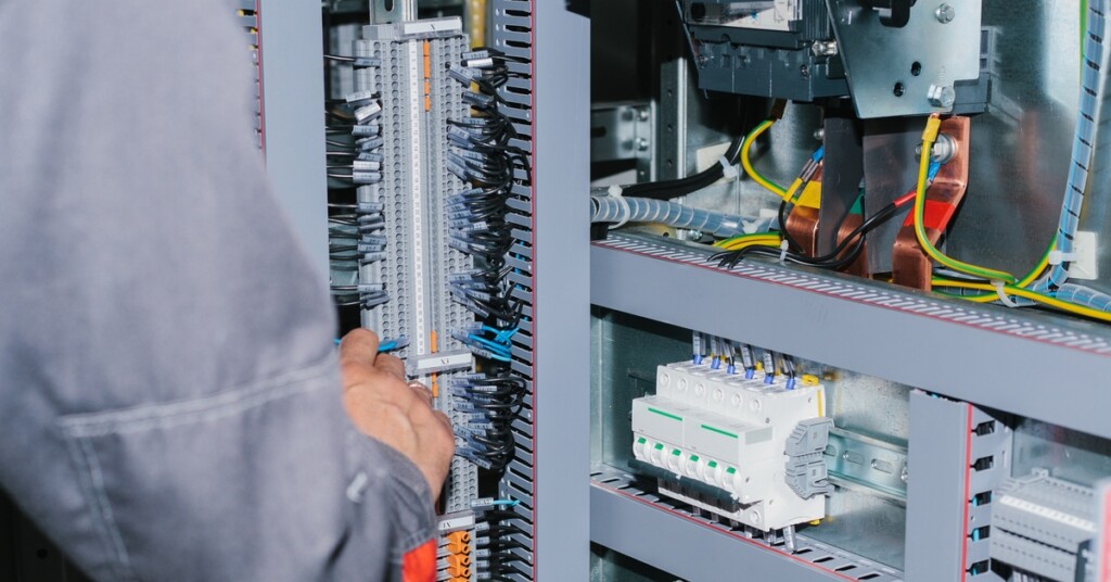 An electrician wearing a long-sleeves shirt checks the internal components inside of a modular electrical enclosure.