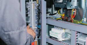 An electrician wearing a long-sleeves shirt checks the internal components inside of a modular electrical enclosure.