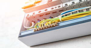 A close-up of an electrical distribution box containing circuit breakers, neatly bundled wires, and a glowing orange light.