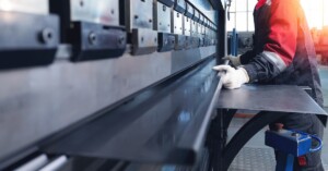 A worker operates a press brake machine to bend a metal sheet in a modern industrial fabrication facility.