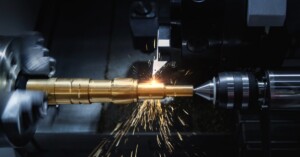 A CNC lathe machine cuts a golden metal shaft, creating bright sparks that spray from the cutting point.