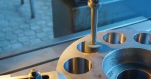 A CNC milling machine grinds circular holes into a metal plate, sending bright sparks across the surface.