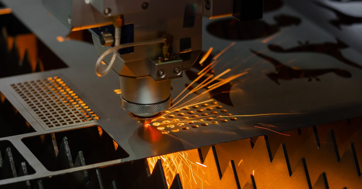 A laser cutting machine cuts a perforated metal sheet as bright sparks scatter across the industrial worktable.